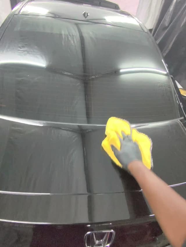 Wiping off polish on the trunk lid of a black Honda Accord coupe