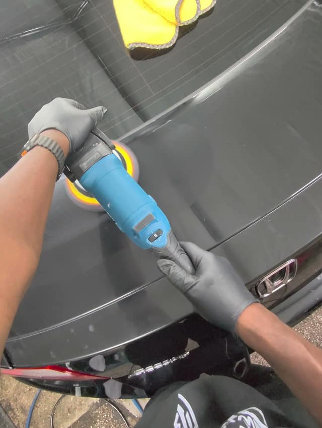Machine polishing the trunk lid of a black Honda Accord coupe