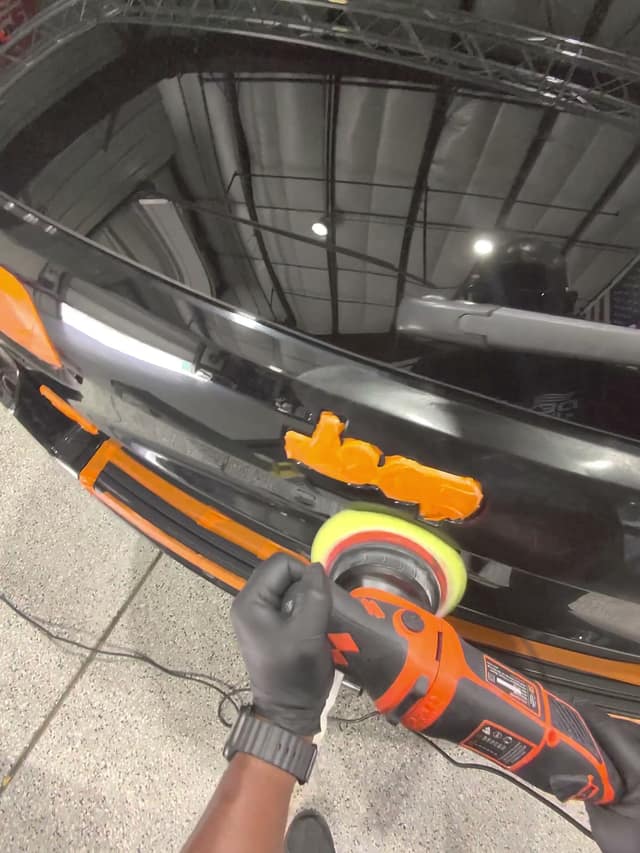 Machine polishing a black Jeep tailgate with the trim taped off, during training